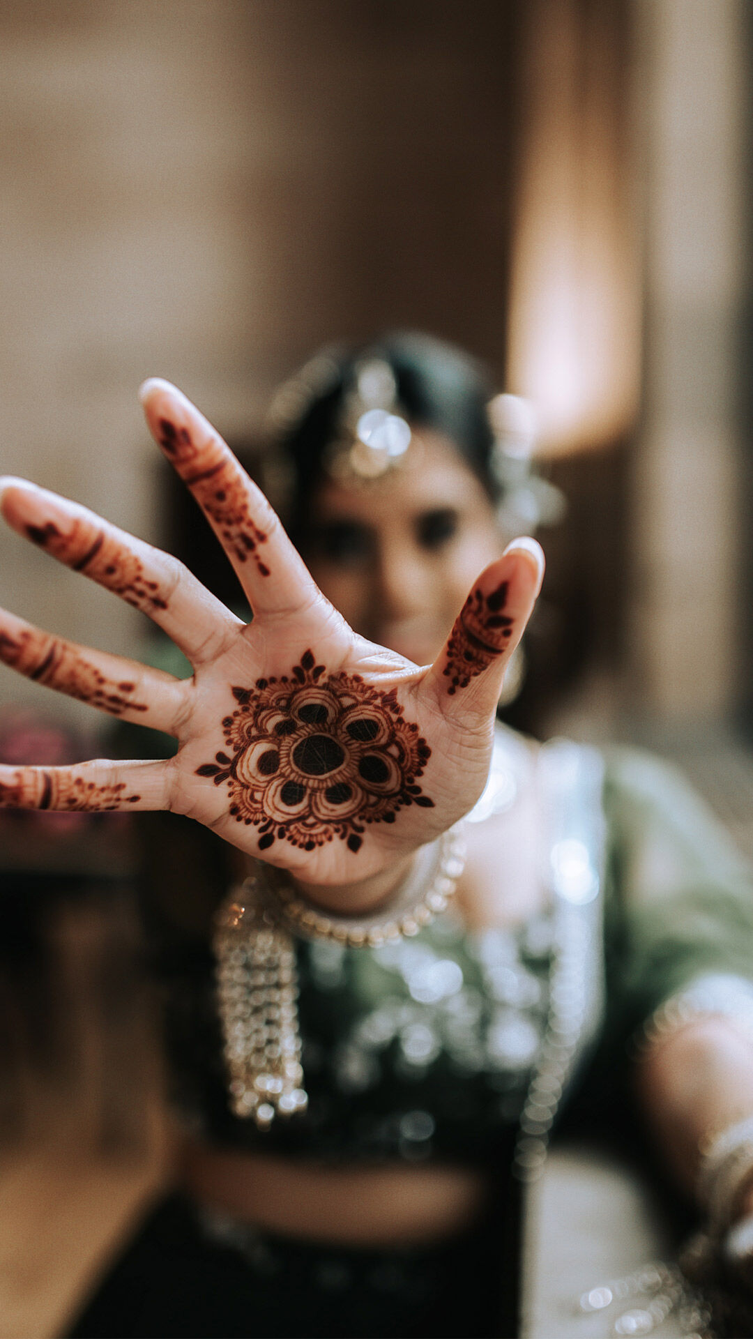 Bride showcasing intricate mehndi design on her palm in a green lehenga during pre-wedding celebration.
